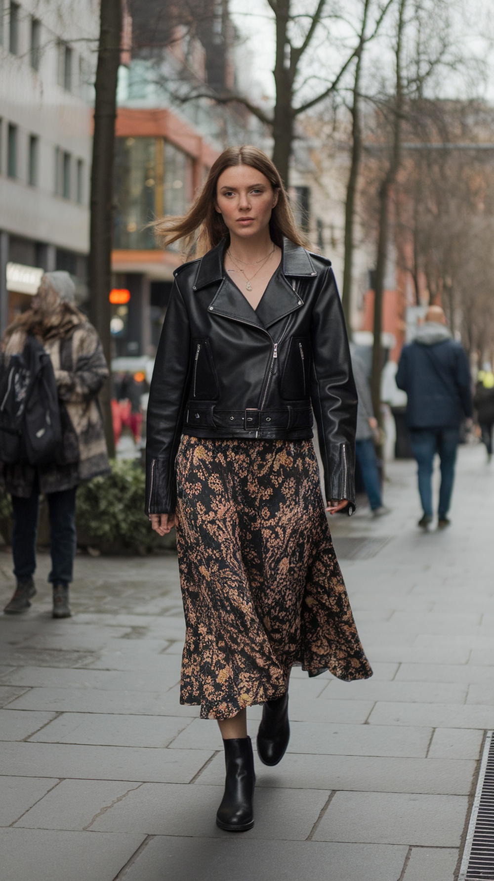A woman wearing a black leather jacket and a floral skirt walking on the street.